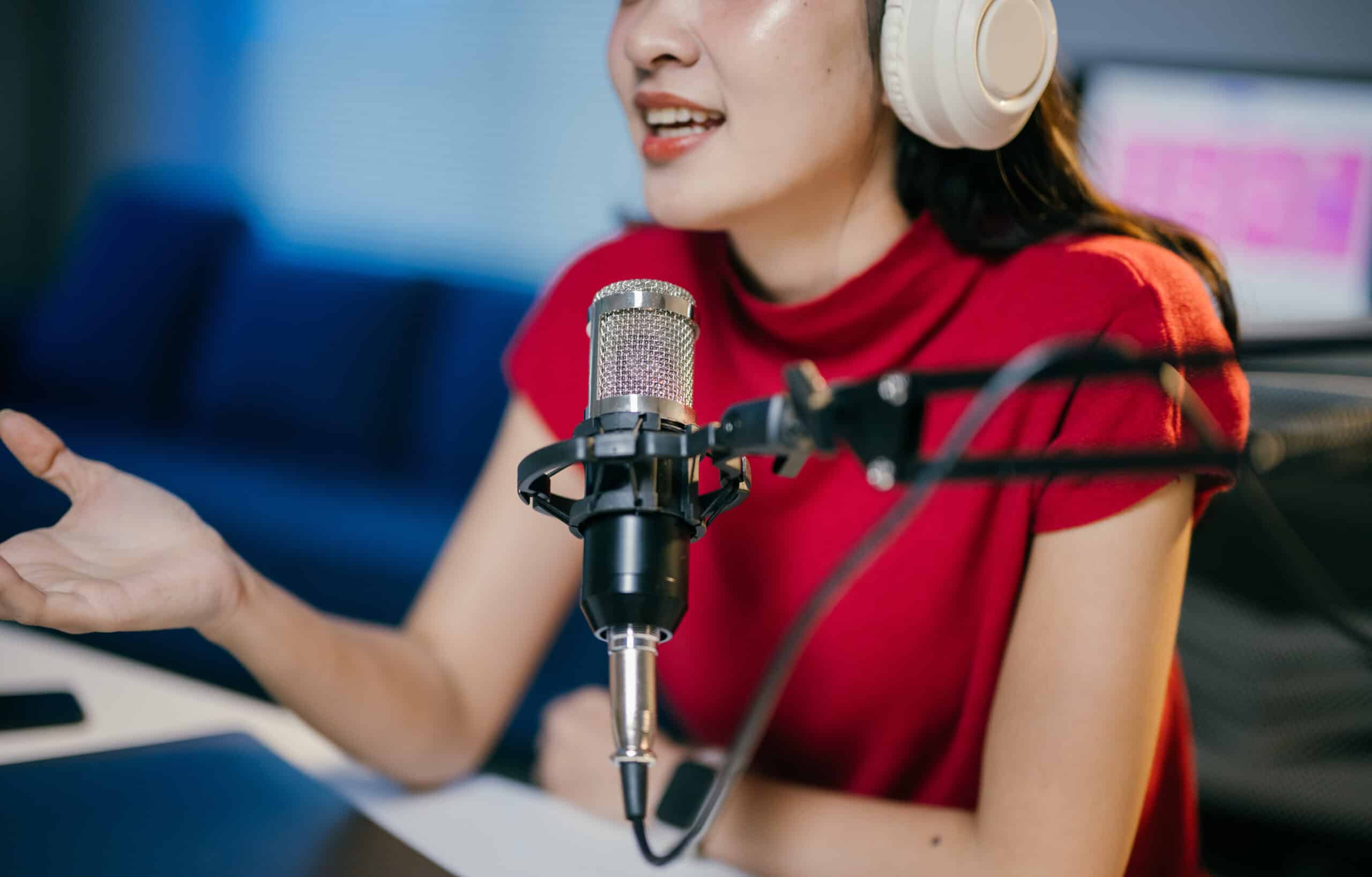 Young woman is recording a podcast in her home studio, speaking into a professional microphone and gesturing with her hand